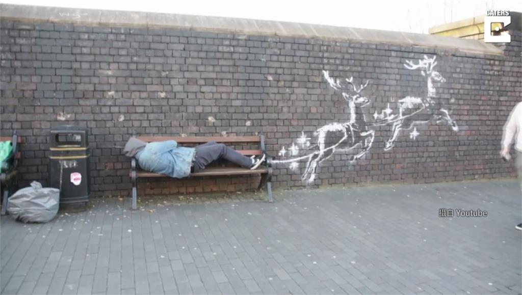 英國知名塗鴉藝術家班克西Banksy，在開設的圍牆飯店旁畫新作，讓遊民化身耶老翱翔天際。圖：網路畫面