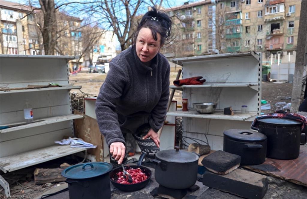 馬里烏波爾郊區，一名婦女在被炮火炸毀的公寓院子裡做飯。圖／翻攝自AP Direct