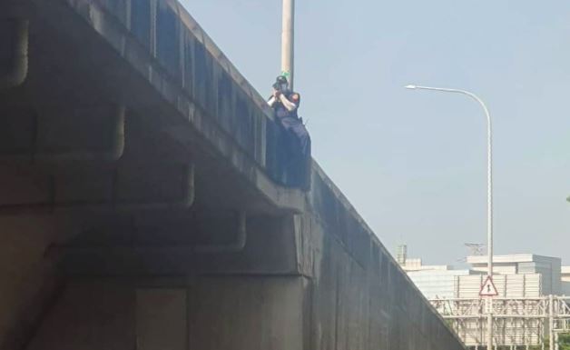 員警跨坐在將近一層樓的高架橋護欄，取締違規。圖／翻攝自爆廢公社二館臉書